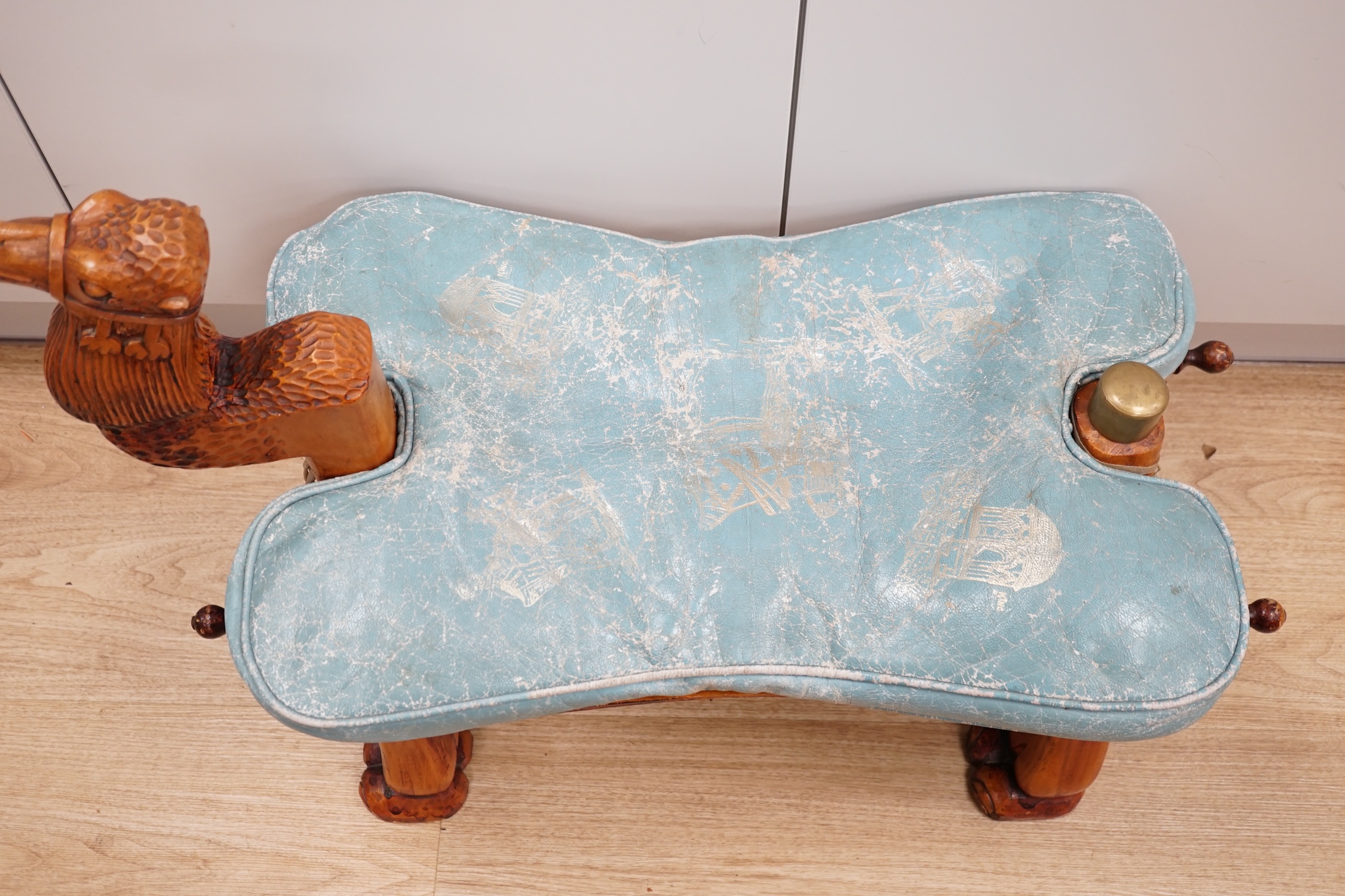 A carved wood foot stool in the form of a camel, blue stamped patterned leather cushion, 56cm high, 71cm wide. Condition - frame good, leather cushion worn